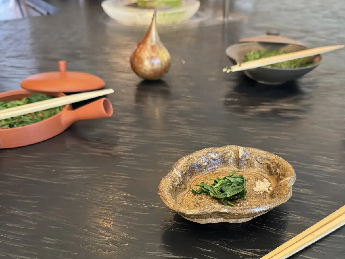 A small rustic ceramic dish holding steeped green tea leaves with a pinch of salt beside them, on the dark counter