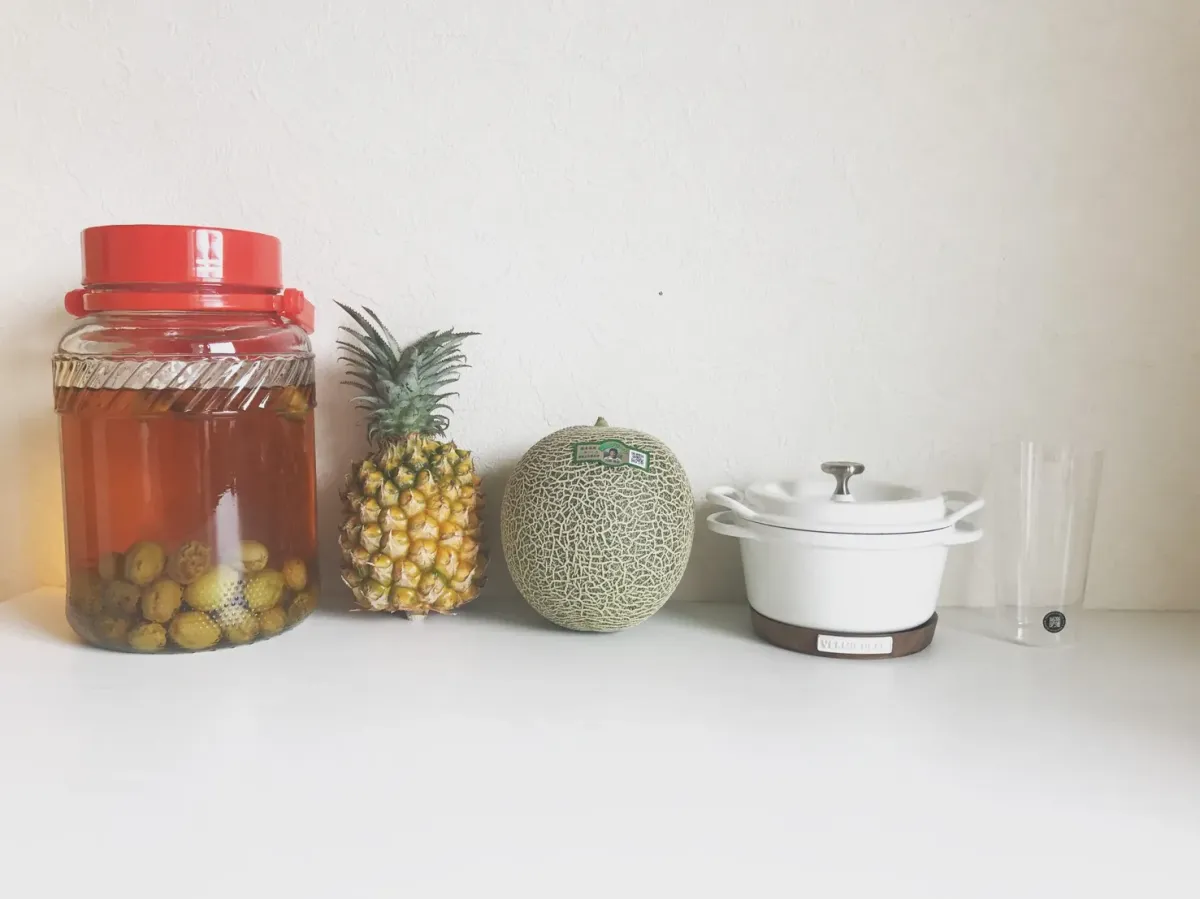 The same jar after aging, the liquid now deep amber, standing on a shelf beside fruit and a cast iron pot