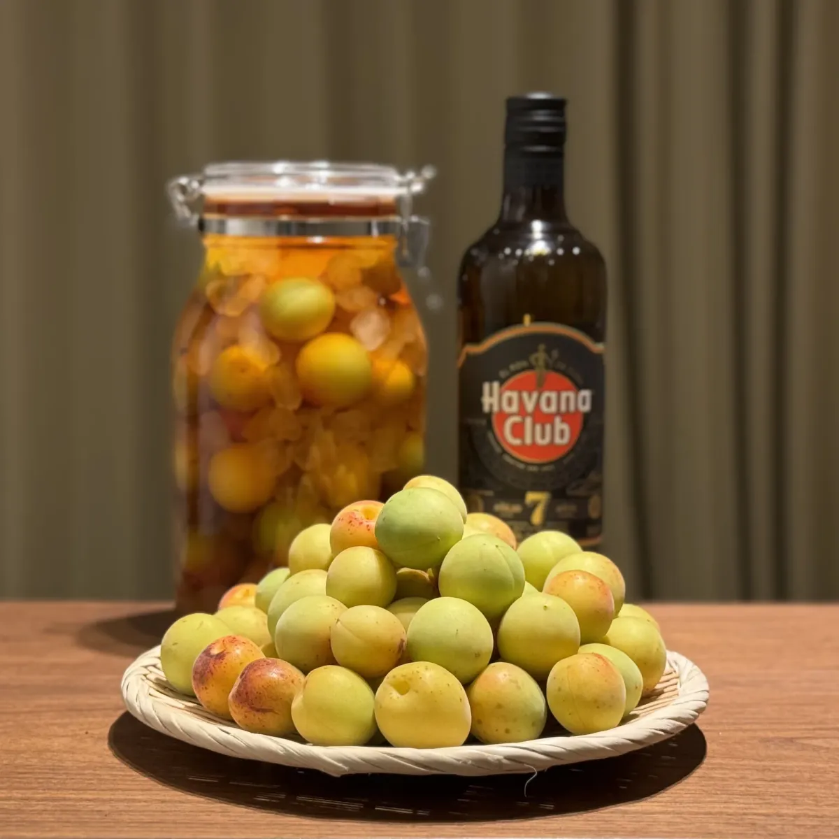 A jar of green plums submerged in dark rum, already deep brown on the day it was made, beside the rum bottle